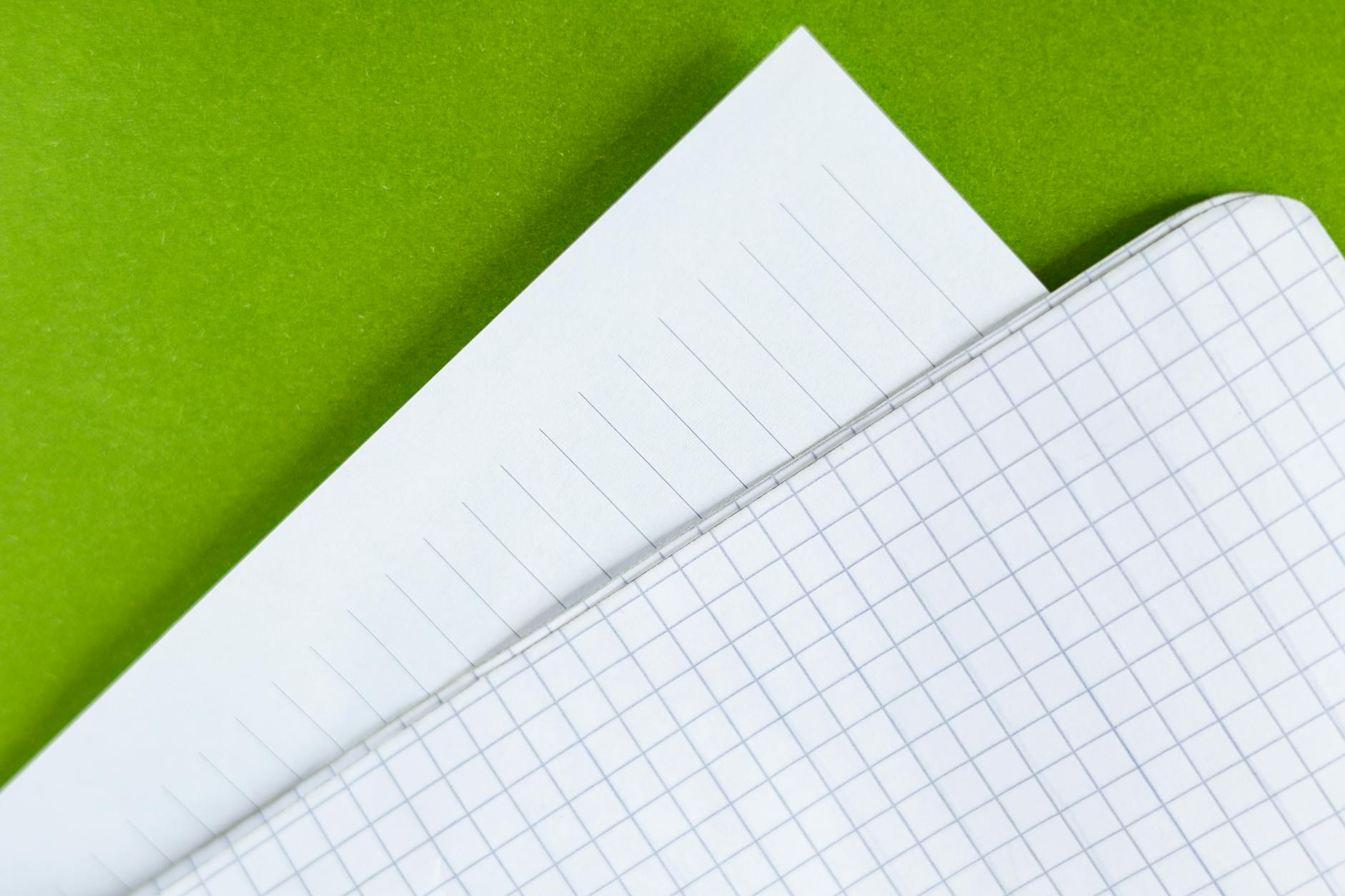 close up of lined and graph paper over green background